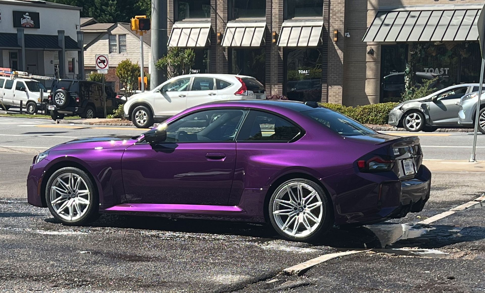 A vibrant metallic purple BMW M2 coupe parked on an asphalt street in front of a commercial building.