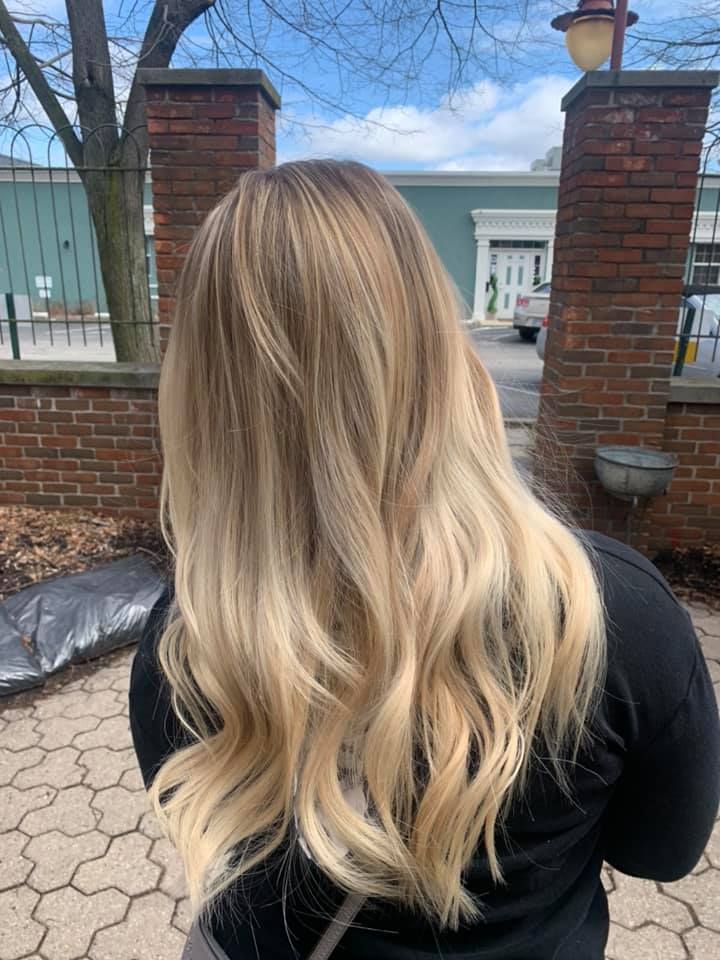 A woman with long blonde hair is standing in front of a brick wall.