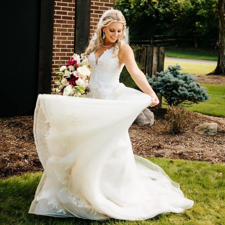A bride in a wedding dress is standing in the grass holding a bouquet of flowers.