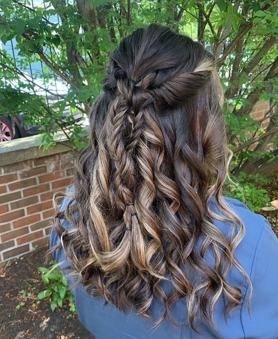 A woman with curly hair is standing in front of a brick wall.