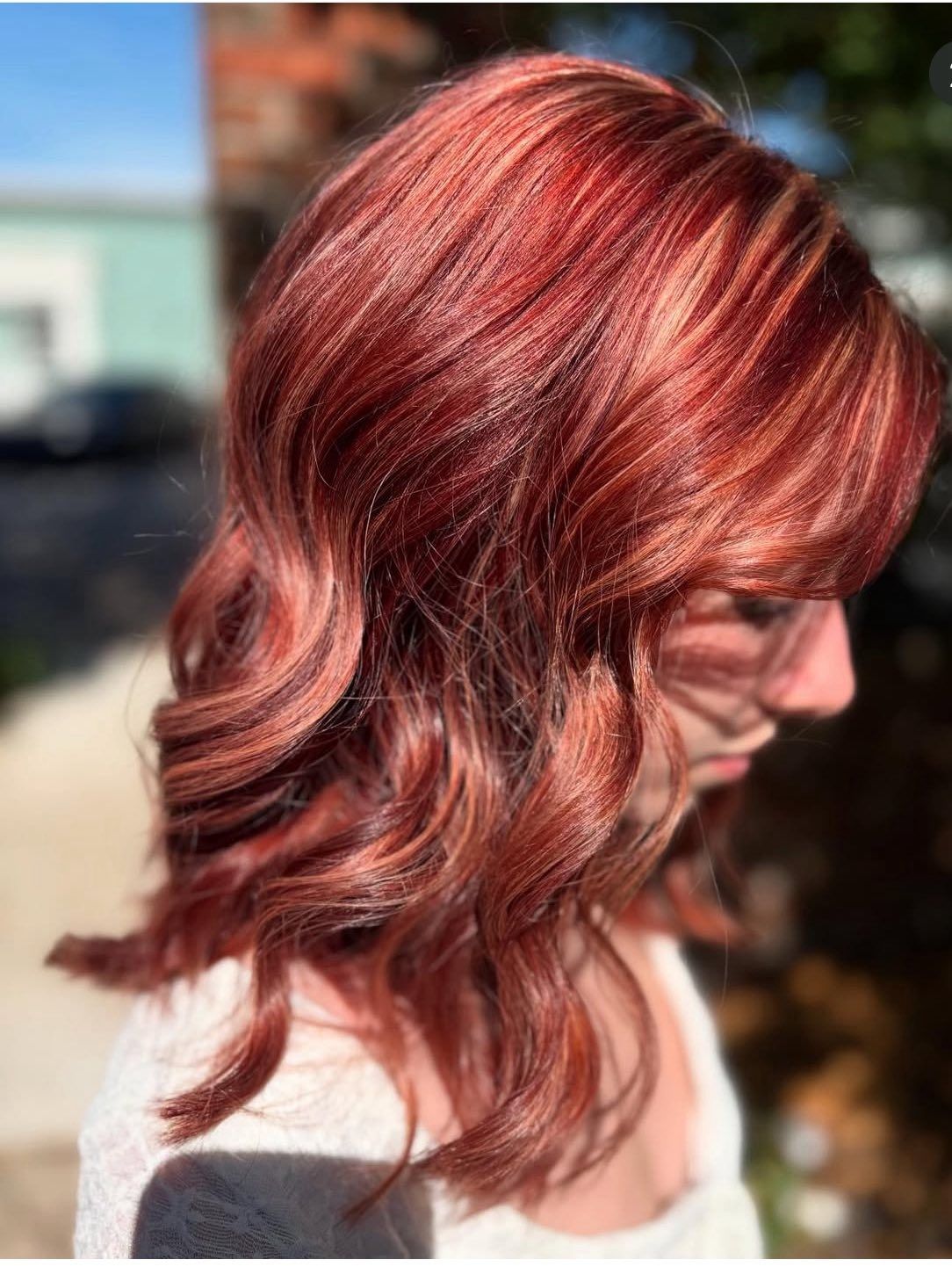Woman with wavy, auburn hair with blonde highlights, outdoors in sunlight.