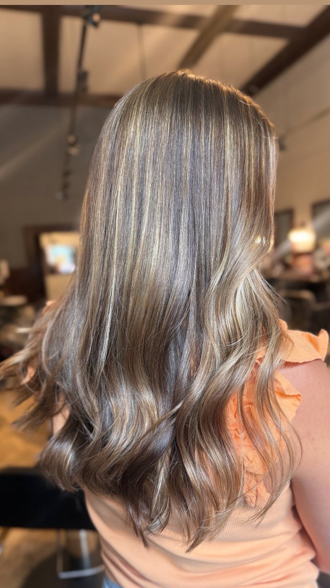Woman with long, layered, highlighted hair, light brown and gold, in salon setting.