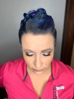 A woman with blue hair is wearing a pink jacket.