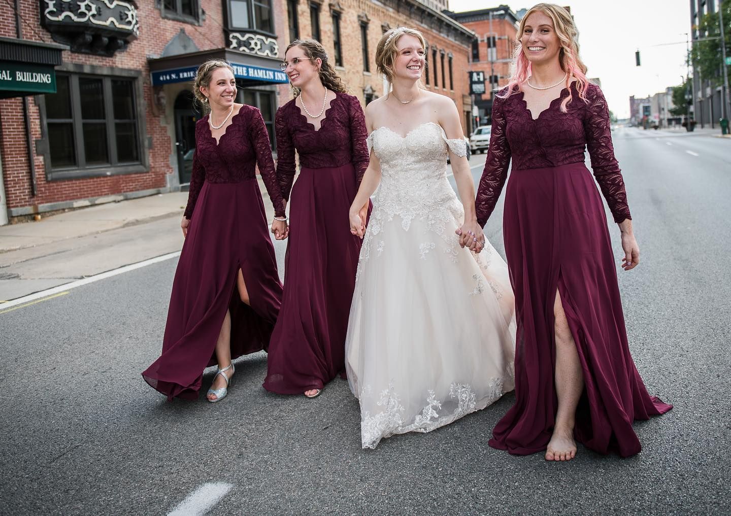 A bride and her bridesmaids are walking down the street holding hands.