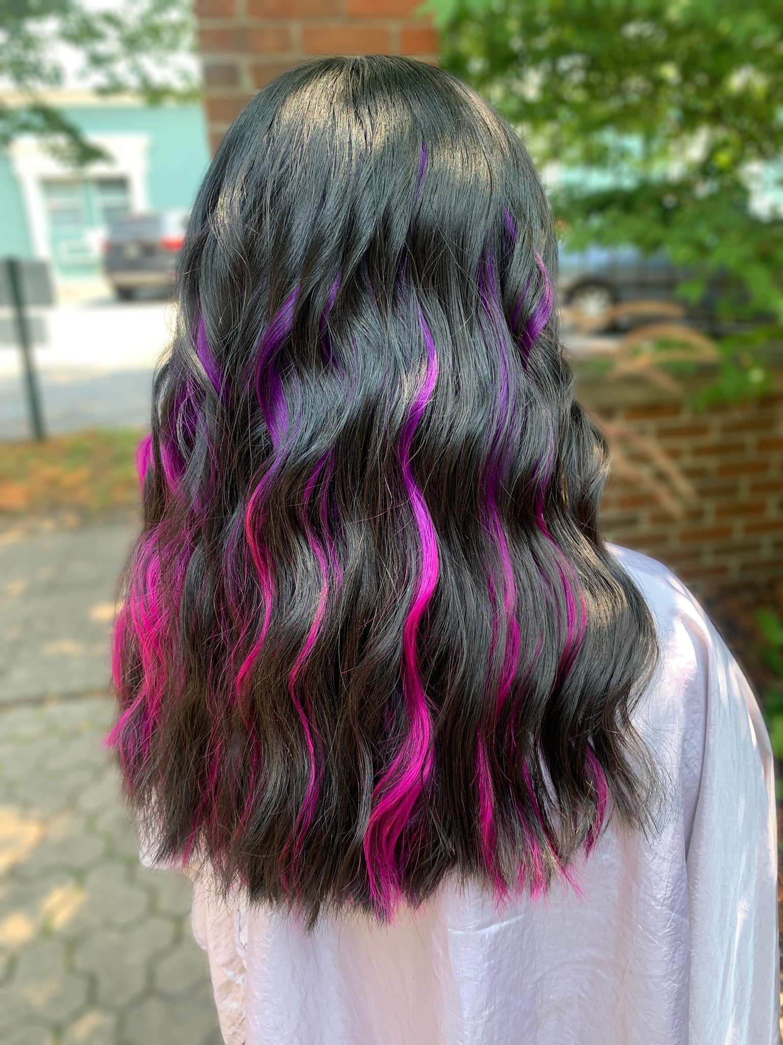 A woman with black hair and pink highlights is standing on a sidewalk.