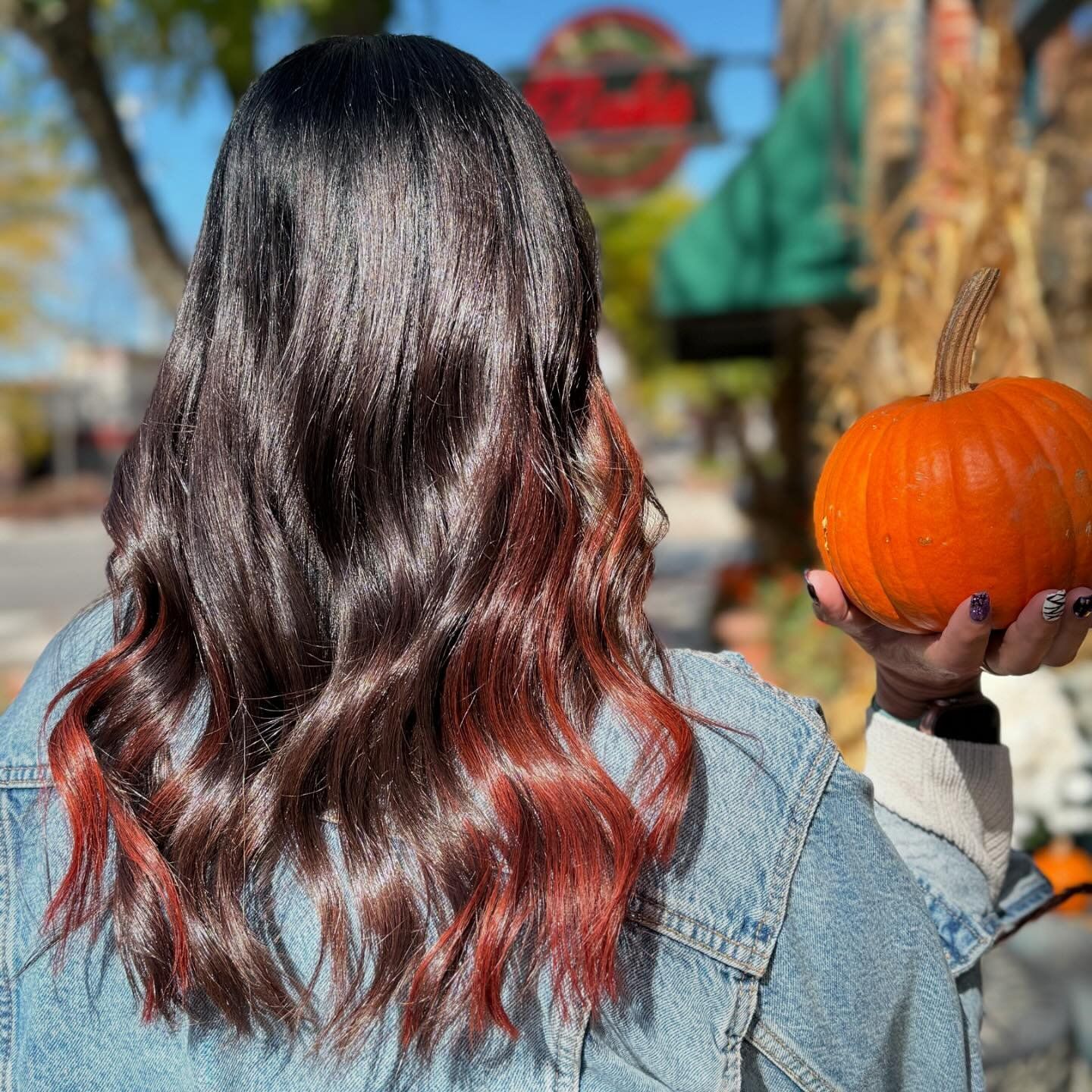 A woman in a denim jacket is holding a pumpkin in her hands.