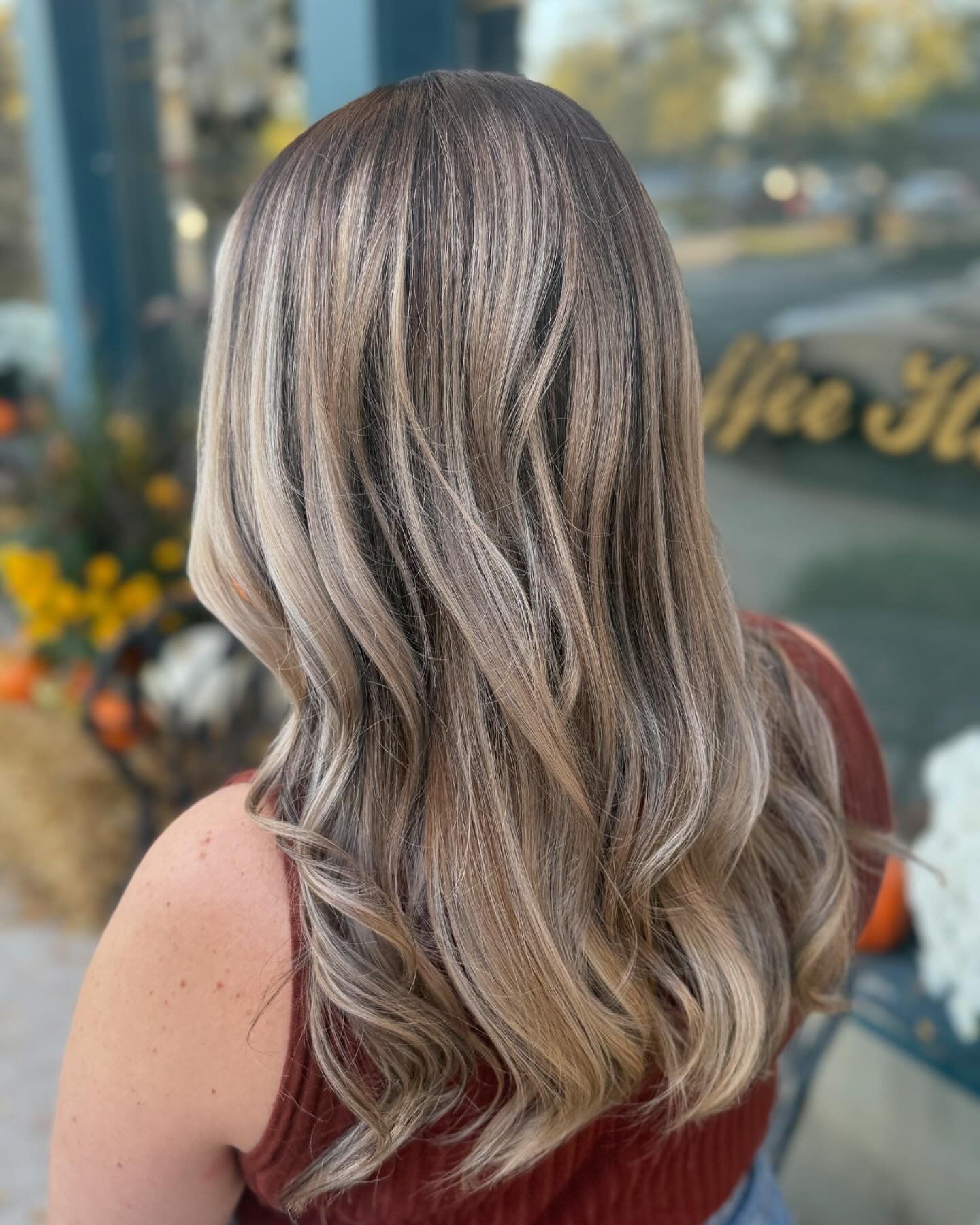 A woman with long blonde hair is standing in front of a window.