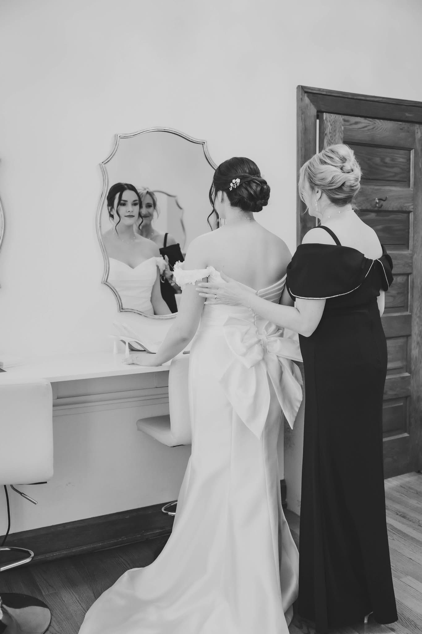 A black and white photo of a bride and her mother getting ready for her wedding.