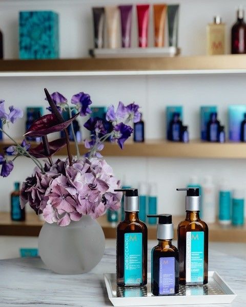 Three bottles of Moroccan Oil are on a tray next to a vase of purple flowers