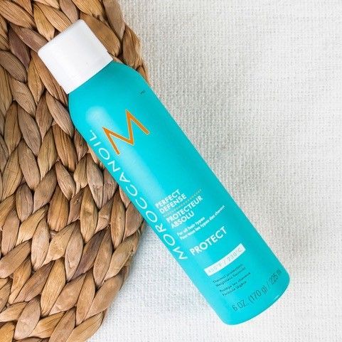 A Moroccan Oil protect spray bottle sits on top of a wicker basket.