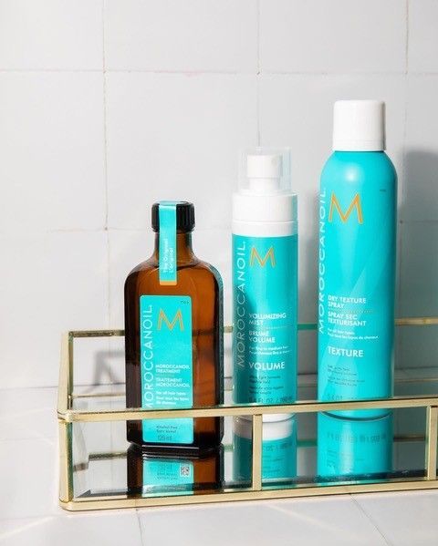 Three bottles of Moroccan Oil are sitting on a glass shelf