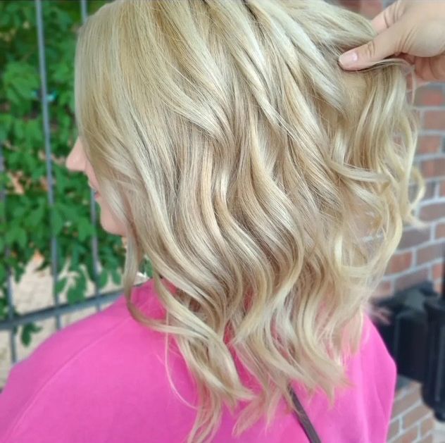 Woman with wavy, light blonde hair, wearing a pink shirt
