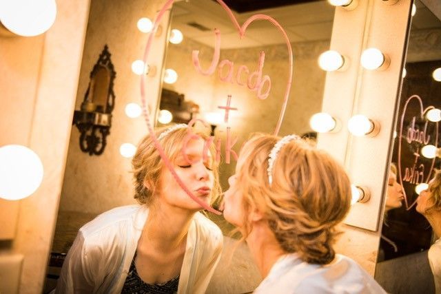 A woman is kissing her reflection in a mirror with a heart drawn on it.
