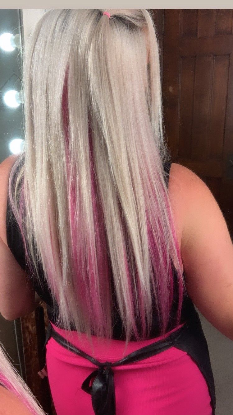 A woman with blonde and pink hair is standing in front of a mirror.