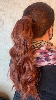 A woman with long red hair is wearing a ponytail and a scarf.
