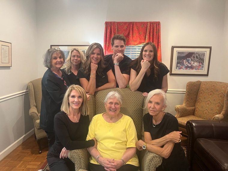 Group of seven people posing indoors in a living room, smiling in front of a red curtain.
