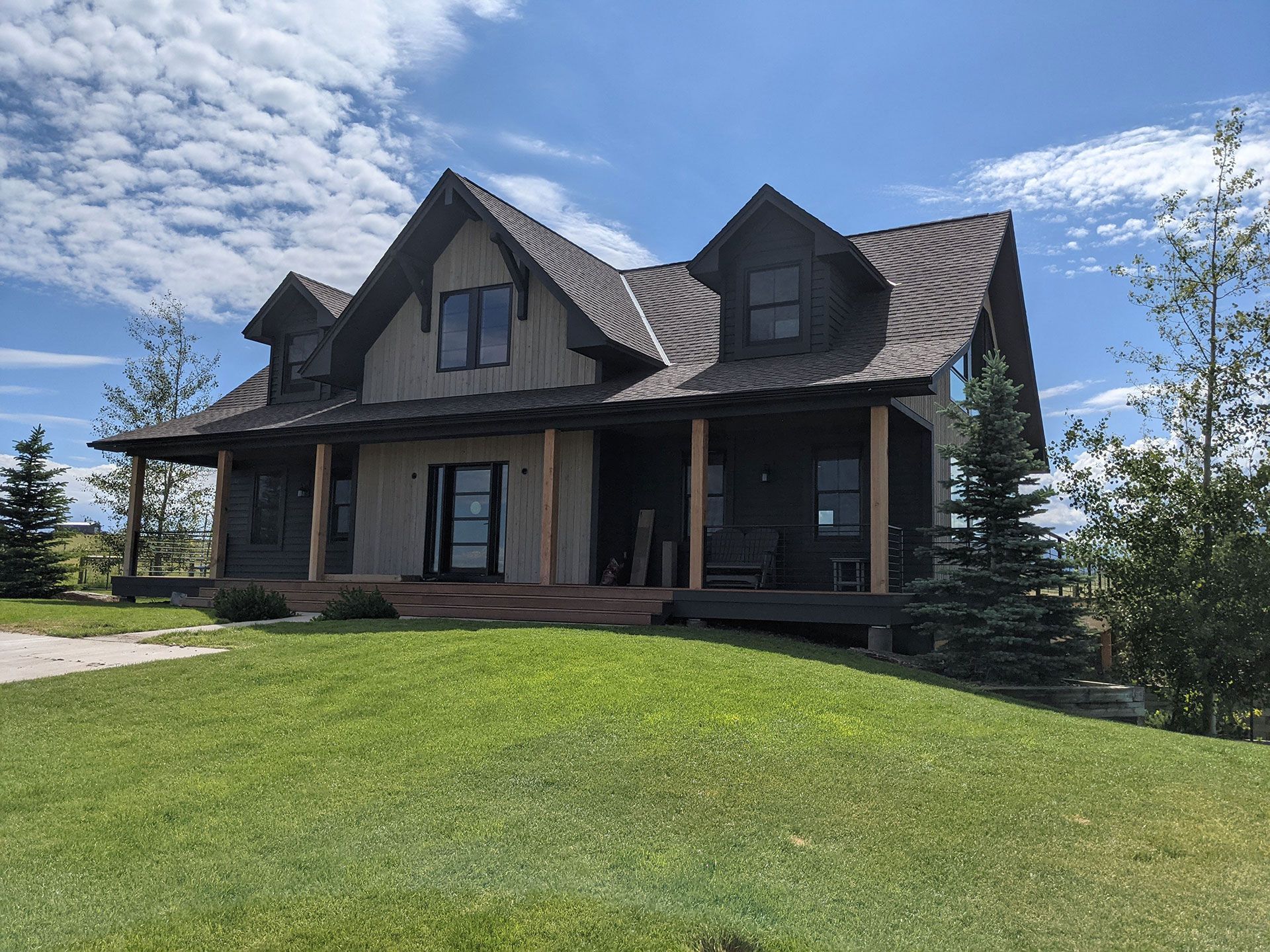 A large house with a large porch is sitting on top of a lush green hill.