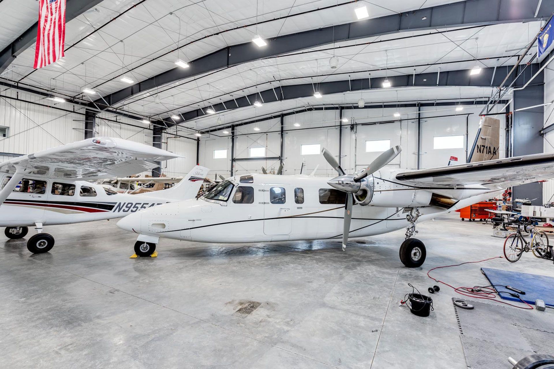 Two small planes are parked in a hangar with an American flag hanging from the ceiling