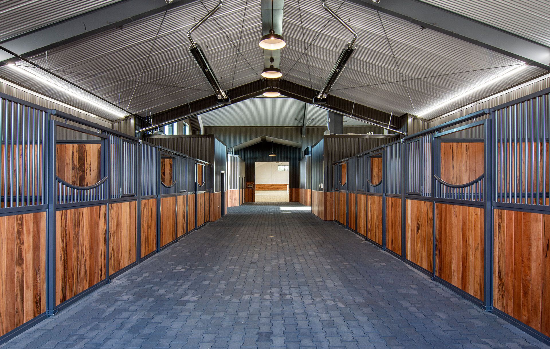 A long hallway in a stable with wooden walls and a metal roof