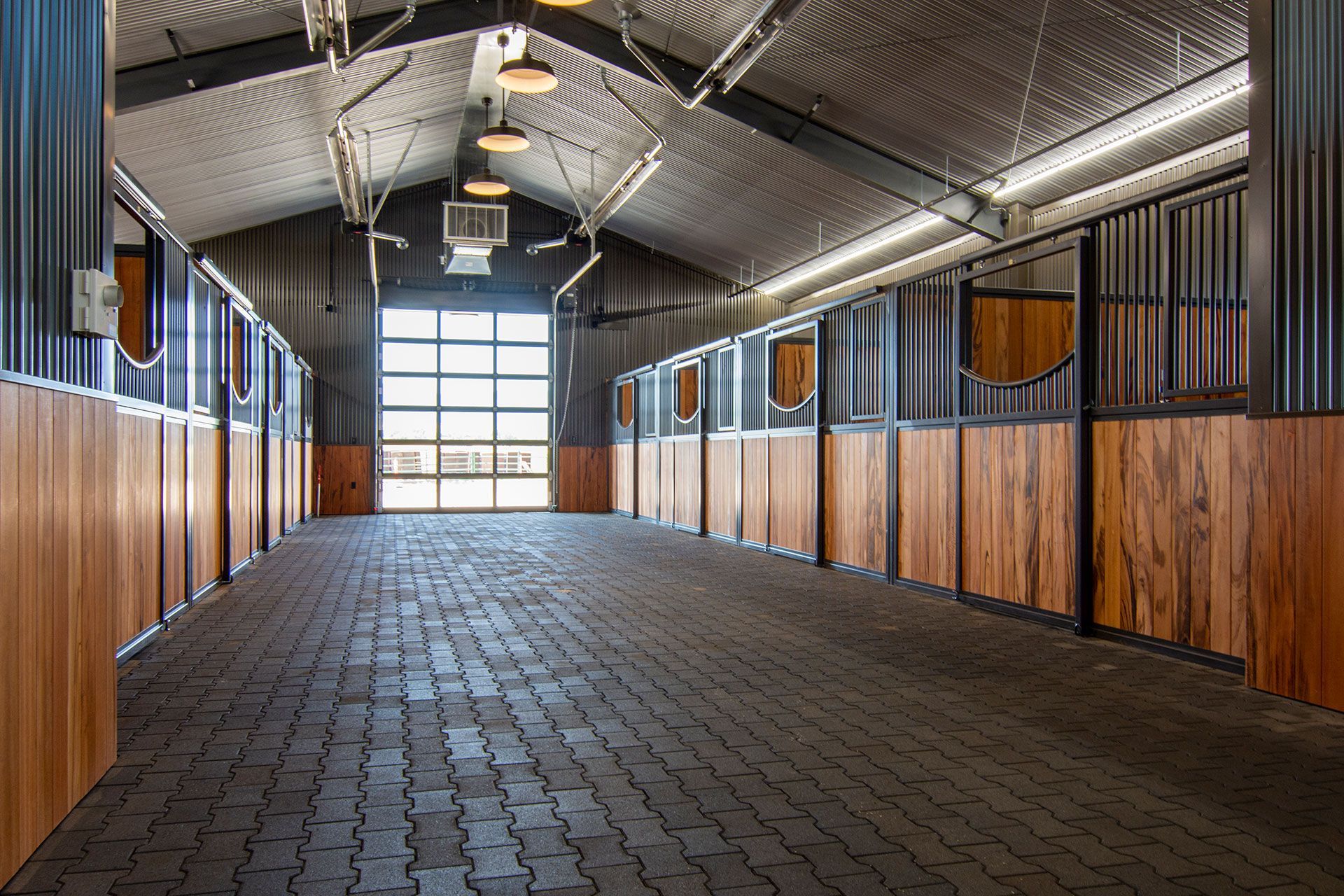 A large empty horse barn with wooden stalls and a large glass door