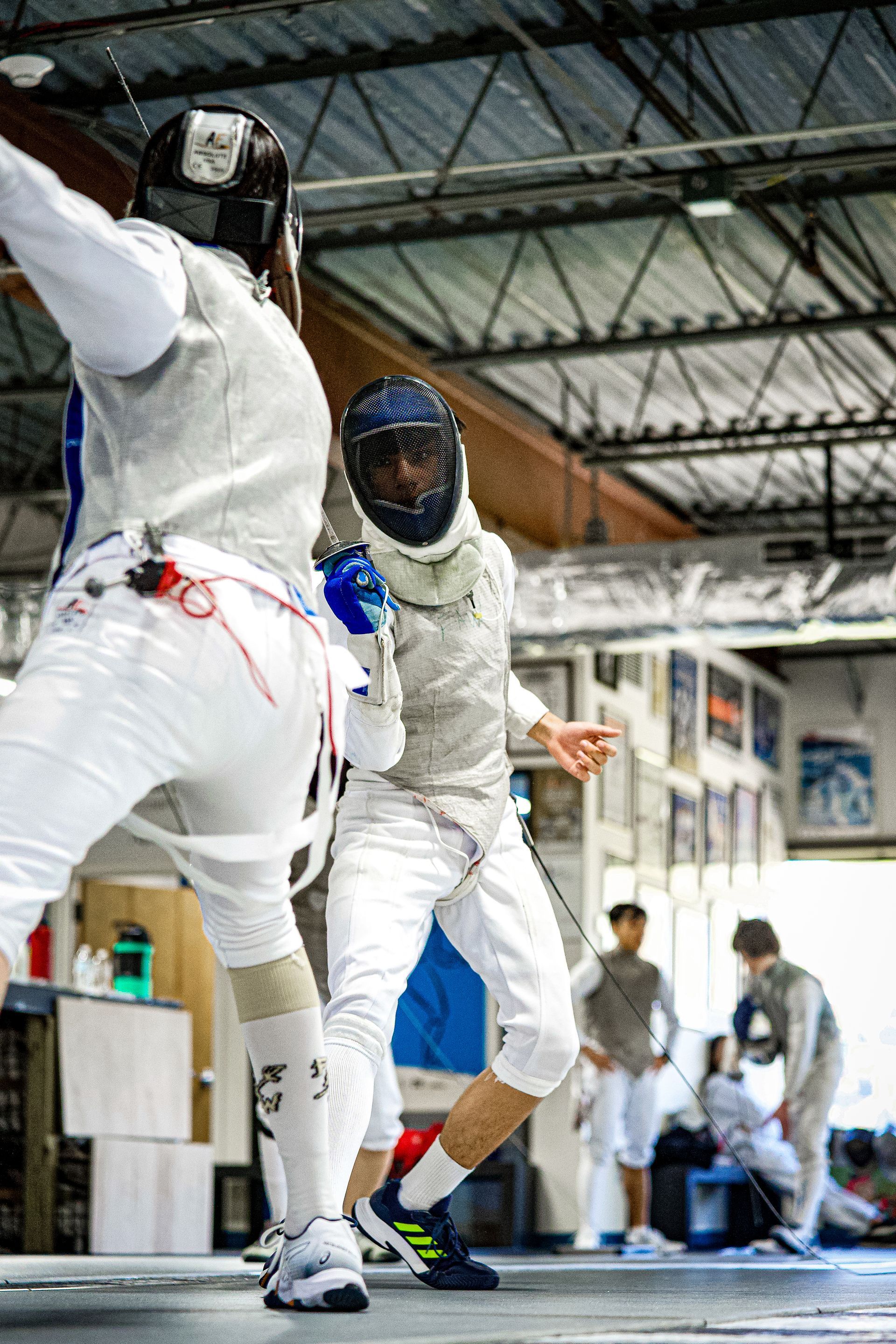 Two men are playing fencing in a gym.