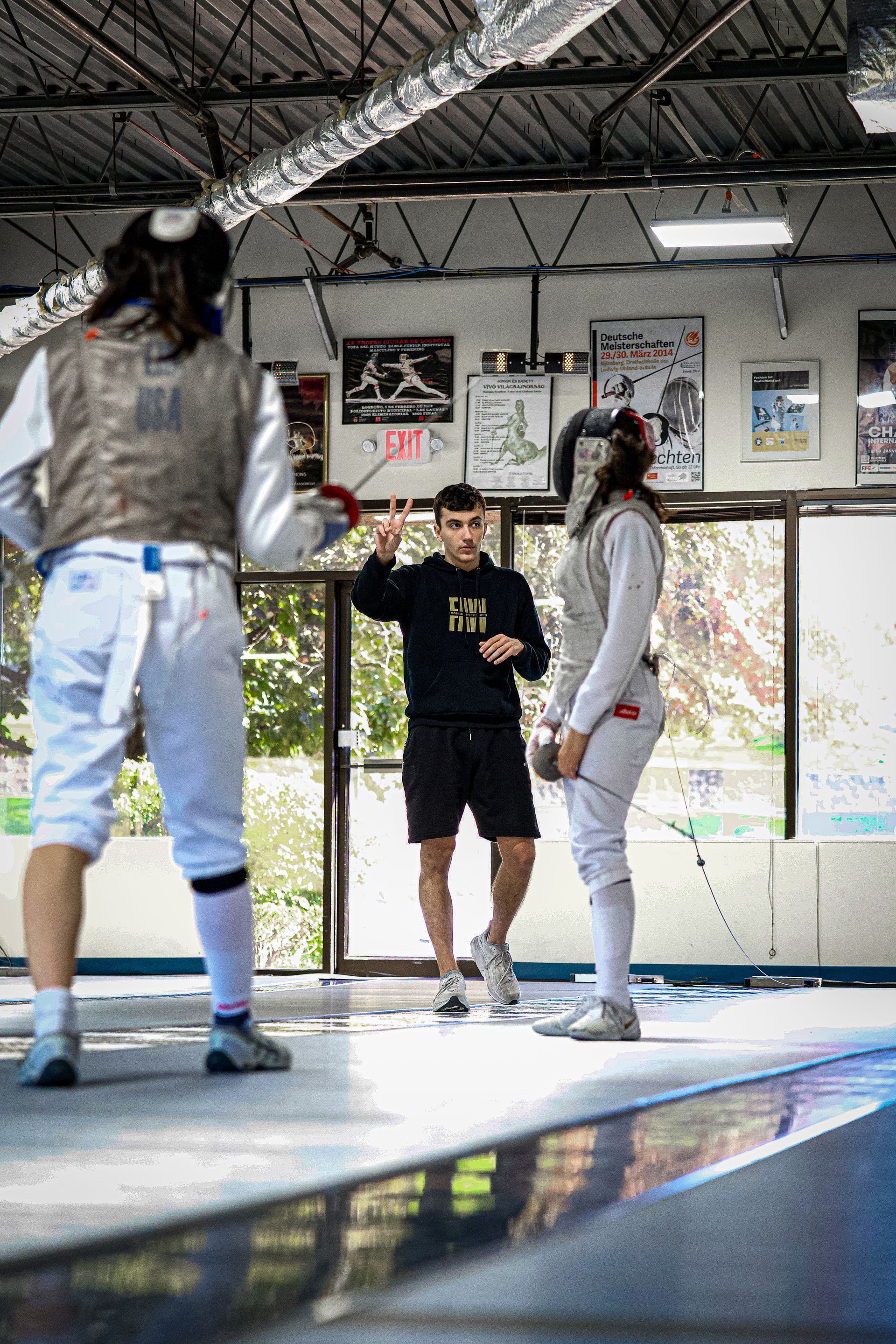 A group of people are standing on a fencing fence in a gym.