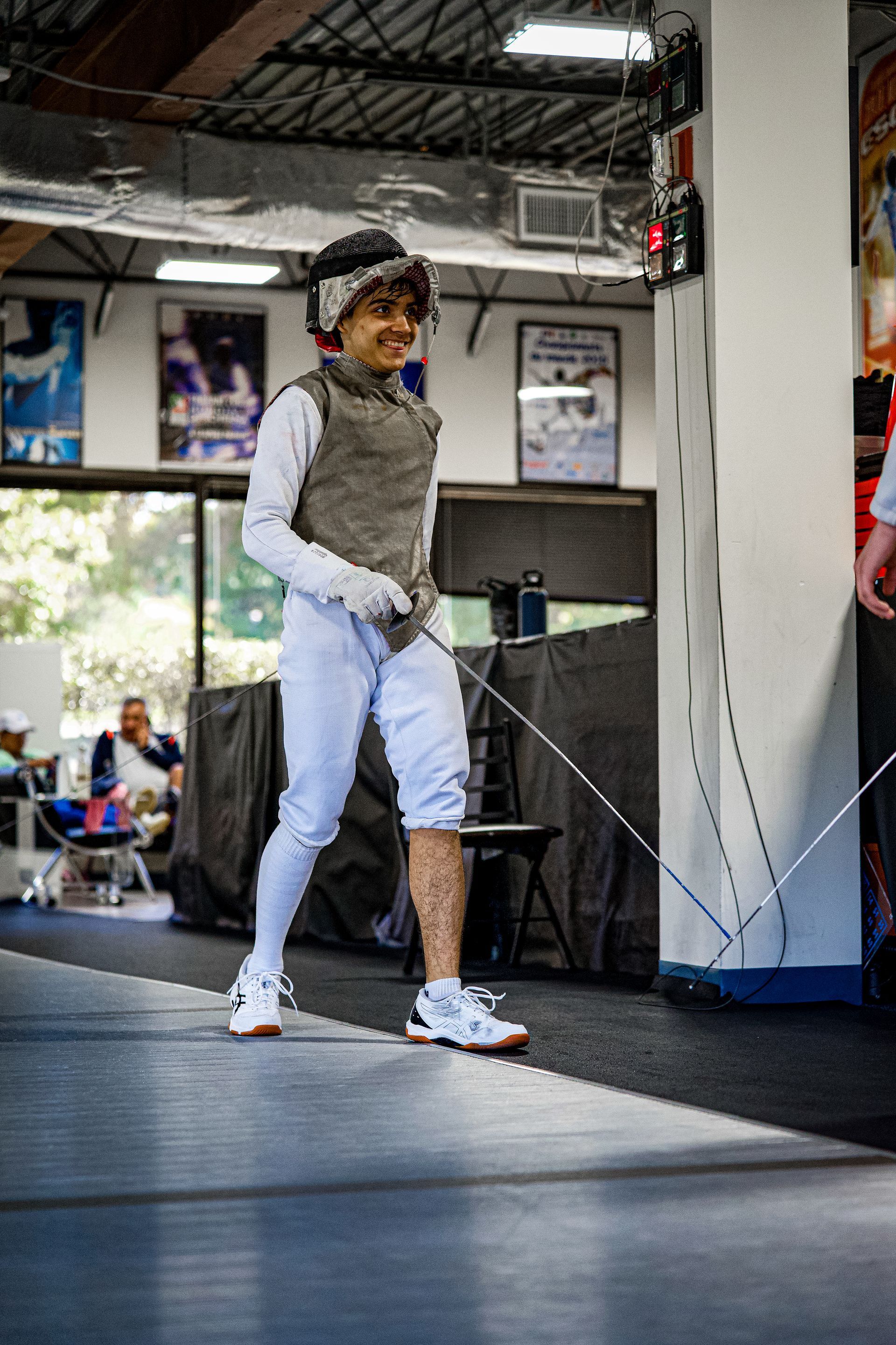 A young boy is practicing fencing in a gym.