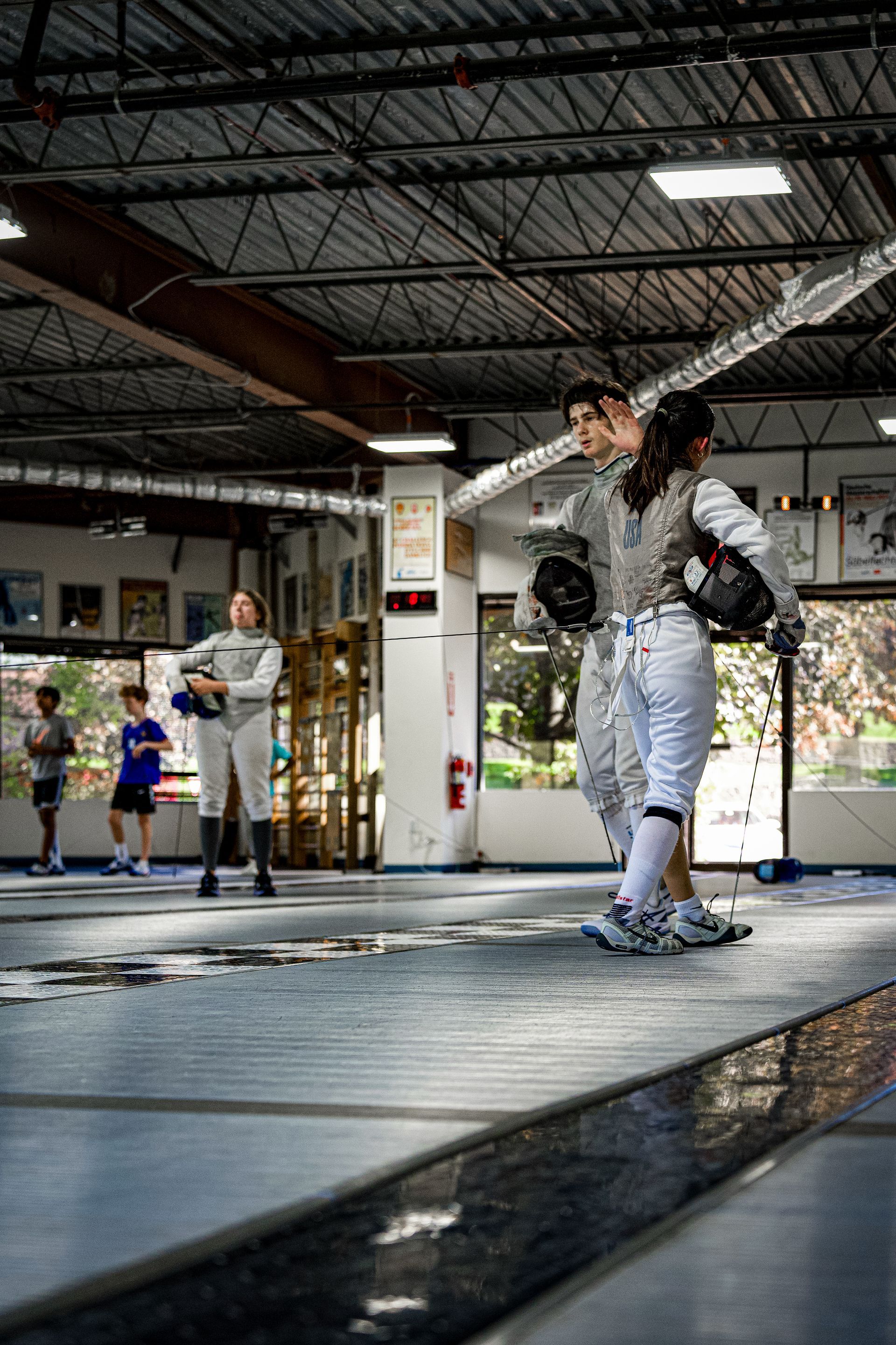 A group of people are fencing in a gym.