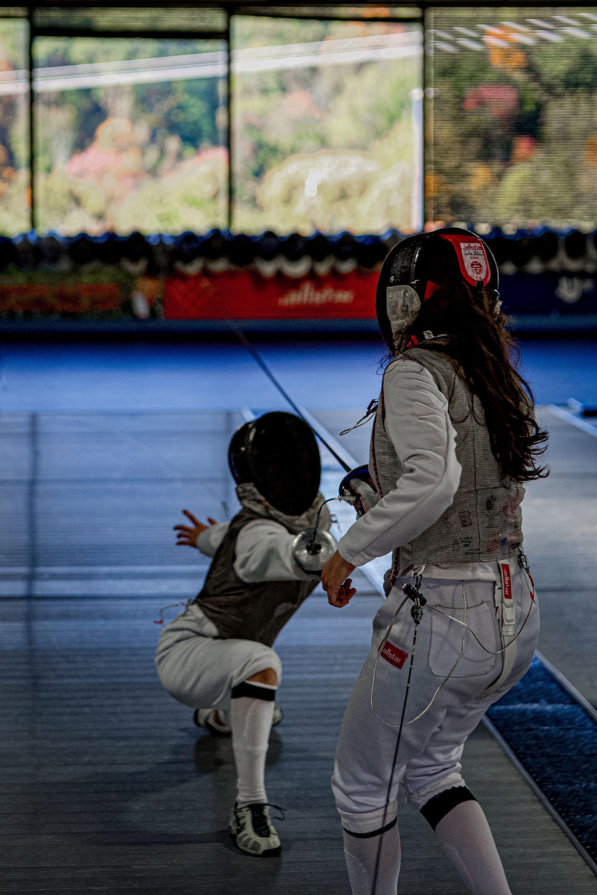 Two young girls are playing fencing in a gym.