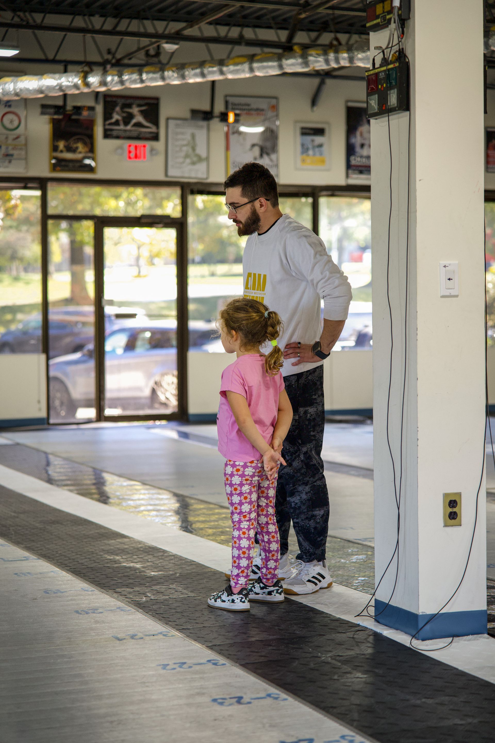 A man and a little girl are standing next to each other in a gym.