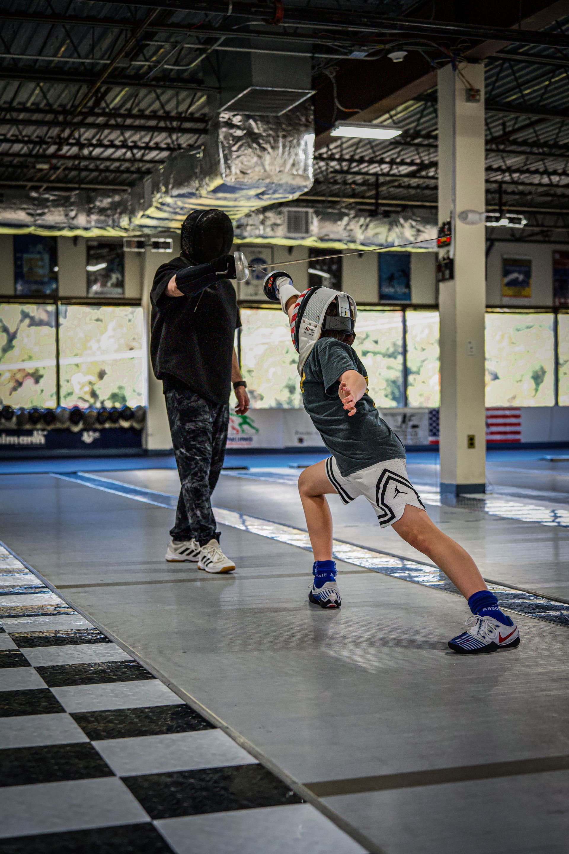A man is standing next to a young boy on a checkered floor in a gym.