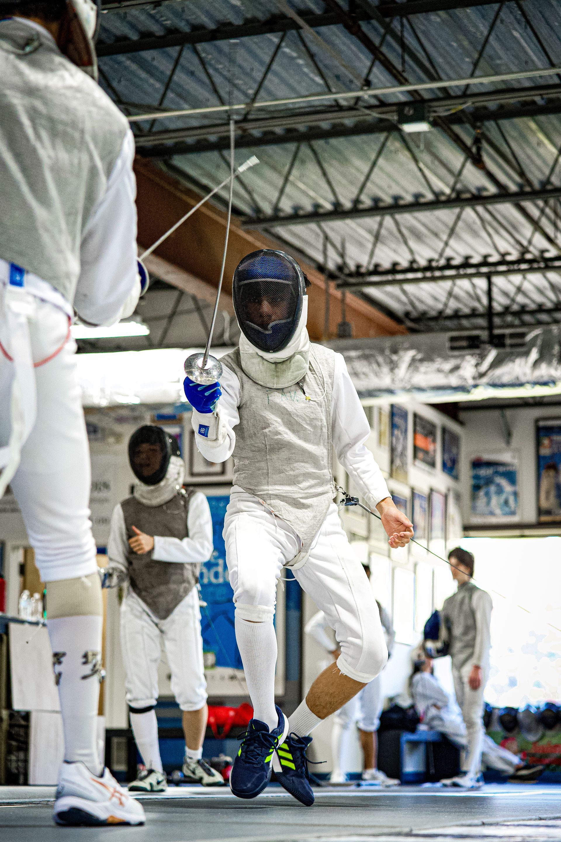 A group of people are fencing in a gym.