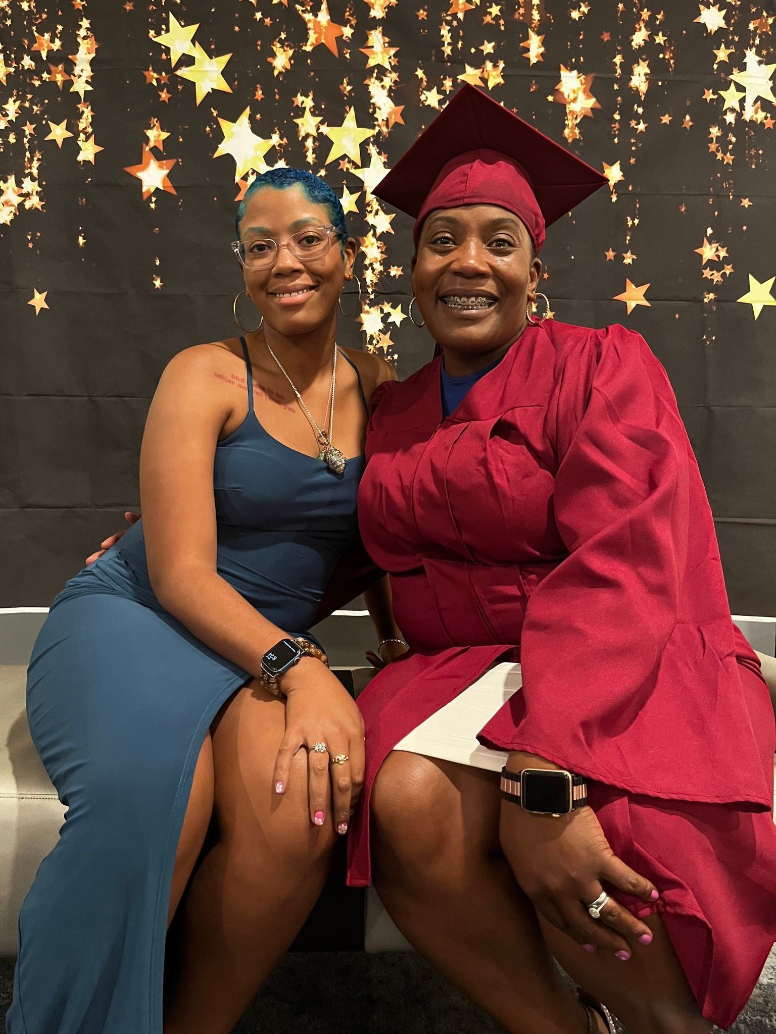 Two women smiling, one in a graduation gown, pose in front of a star-studded backdrop.