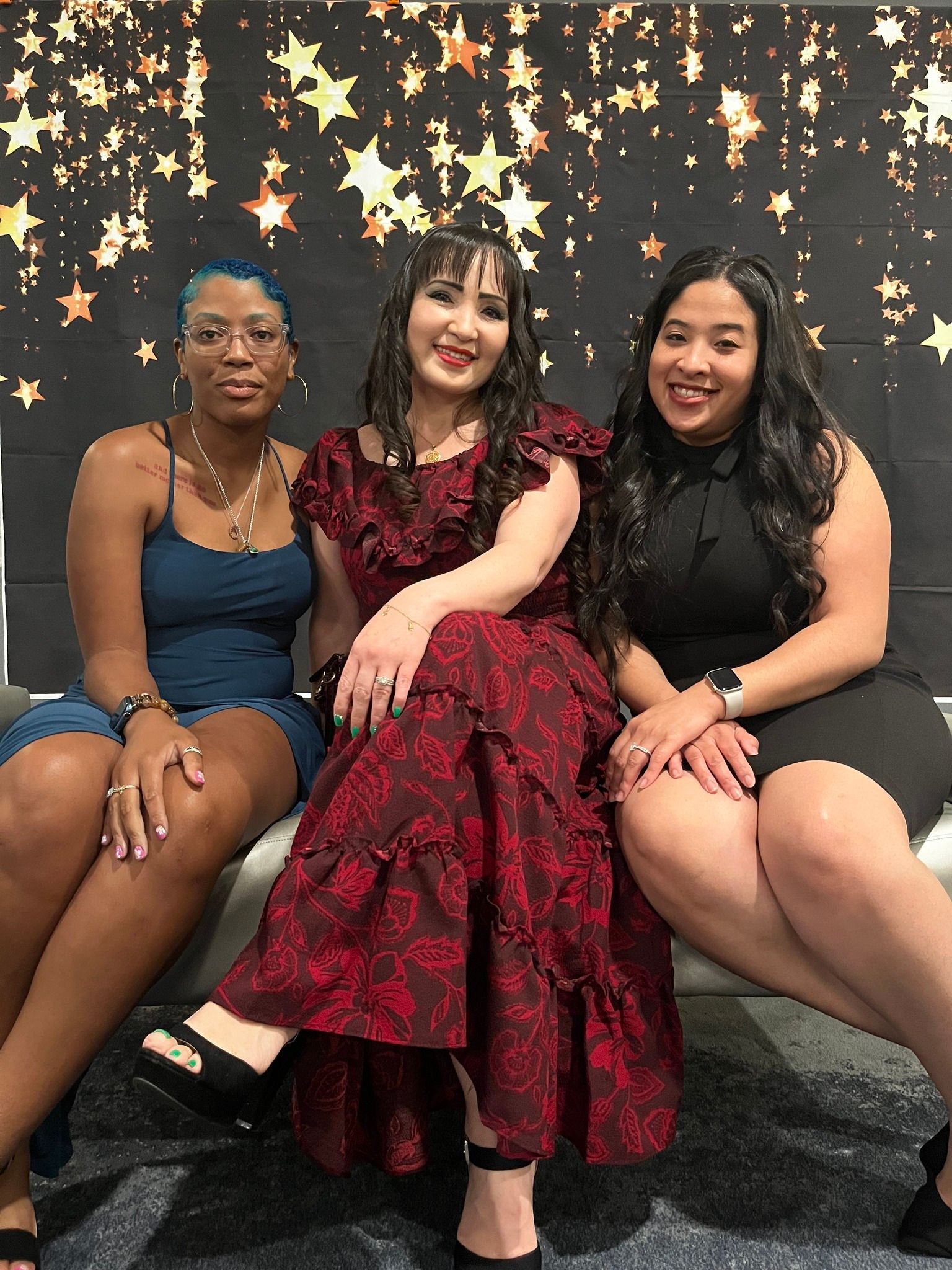 Three people smiling, sitting on a bench in front of a star backdrop.