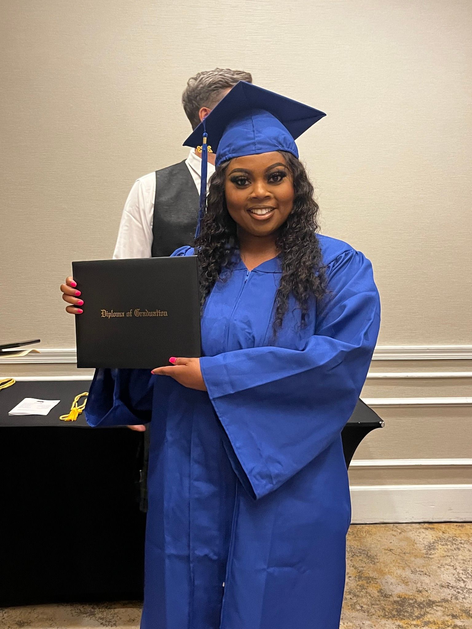 Woman in blue graduation gown holding diploma, smiling.