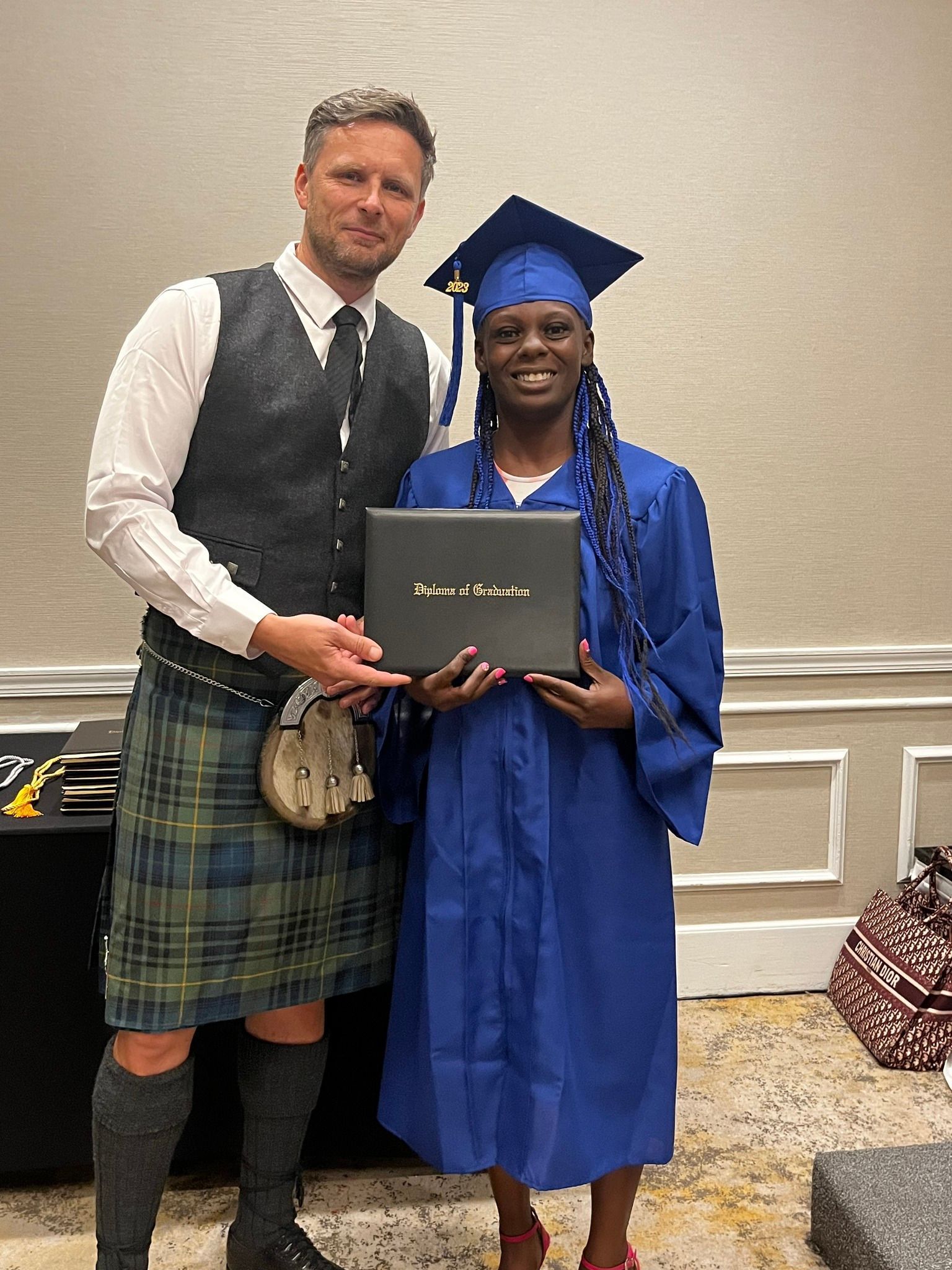 Man in kilt and woman in graduation gown hold diploma.