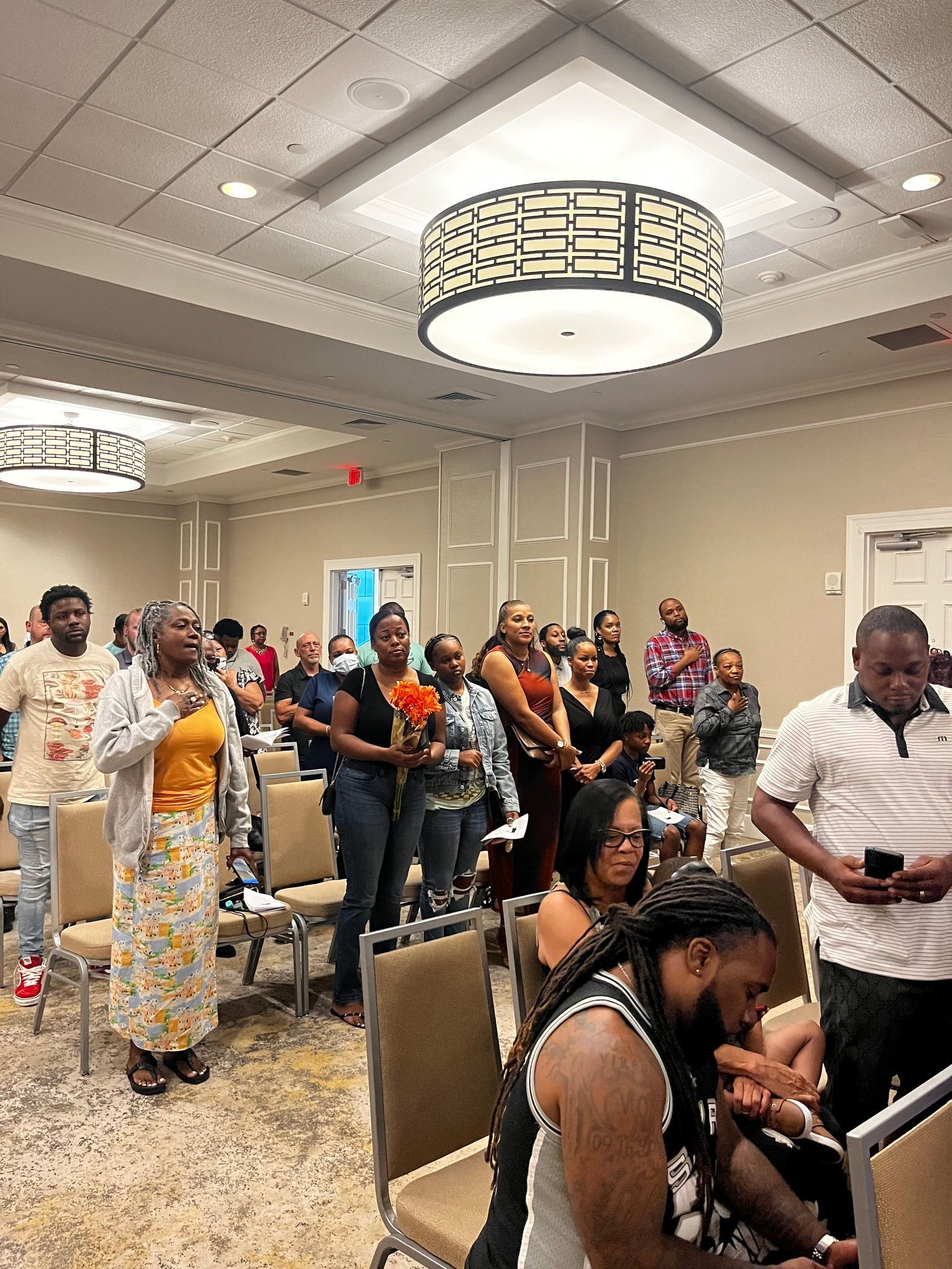 People gathered in a room, some standing with hands raised, lit by overhead lighting.