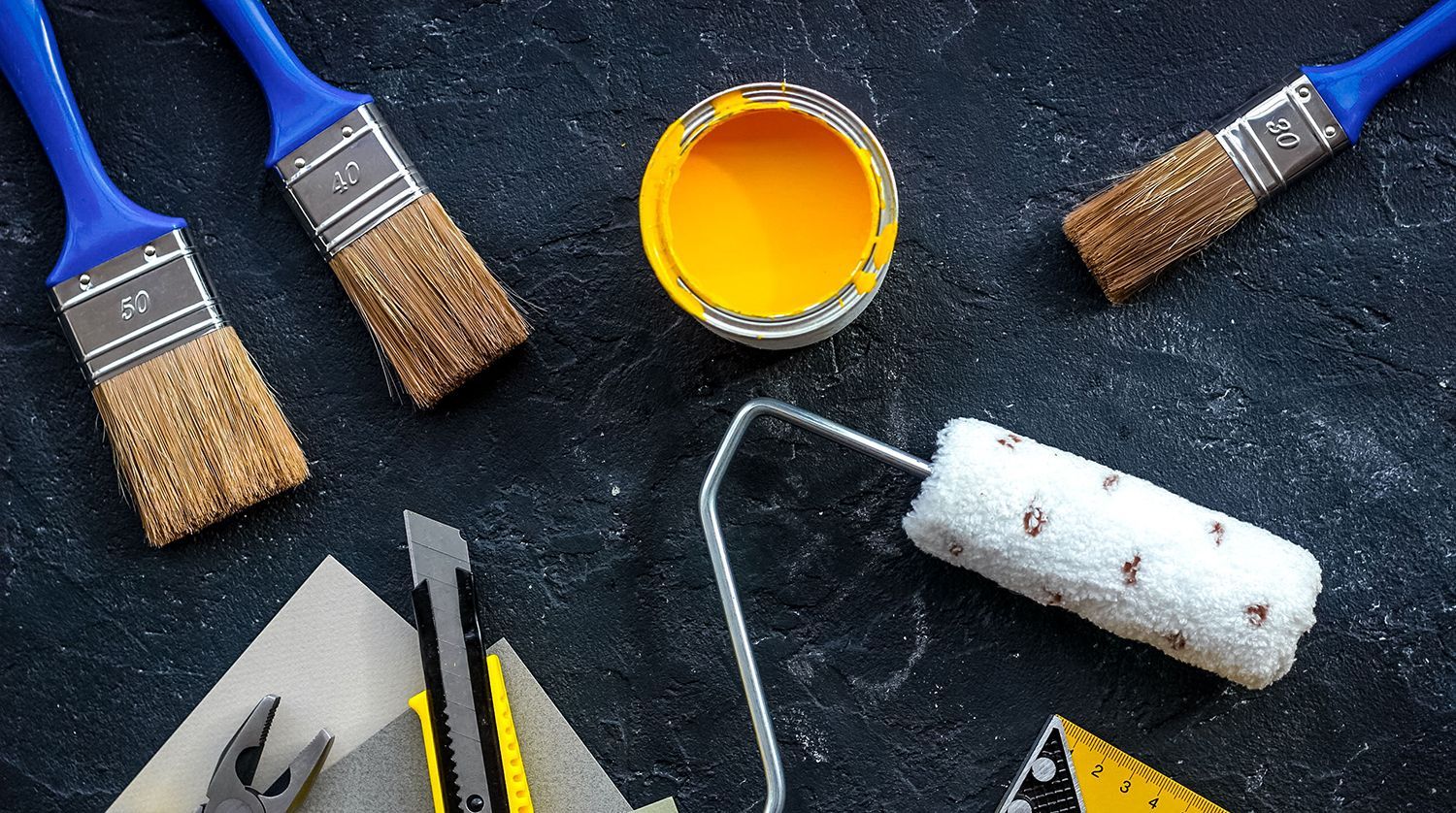 Painting supplies including three blue brushes, a can of yellow paint, a paint roller, and tools on a dark background.
