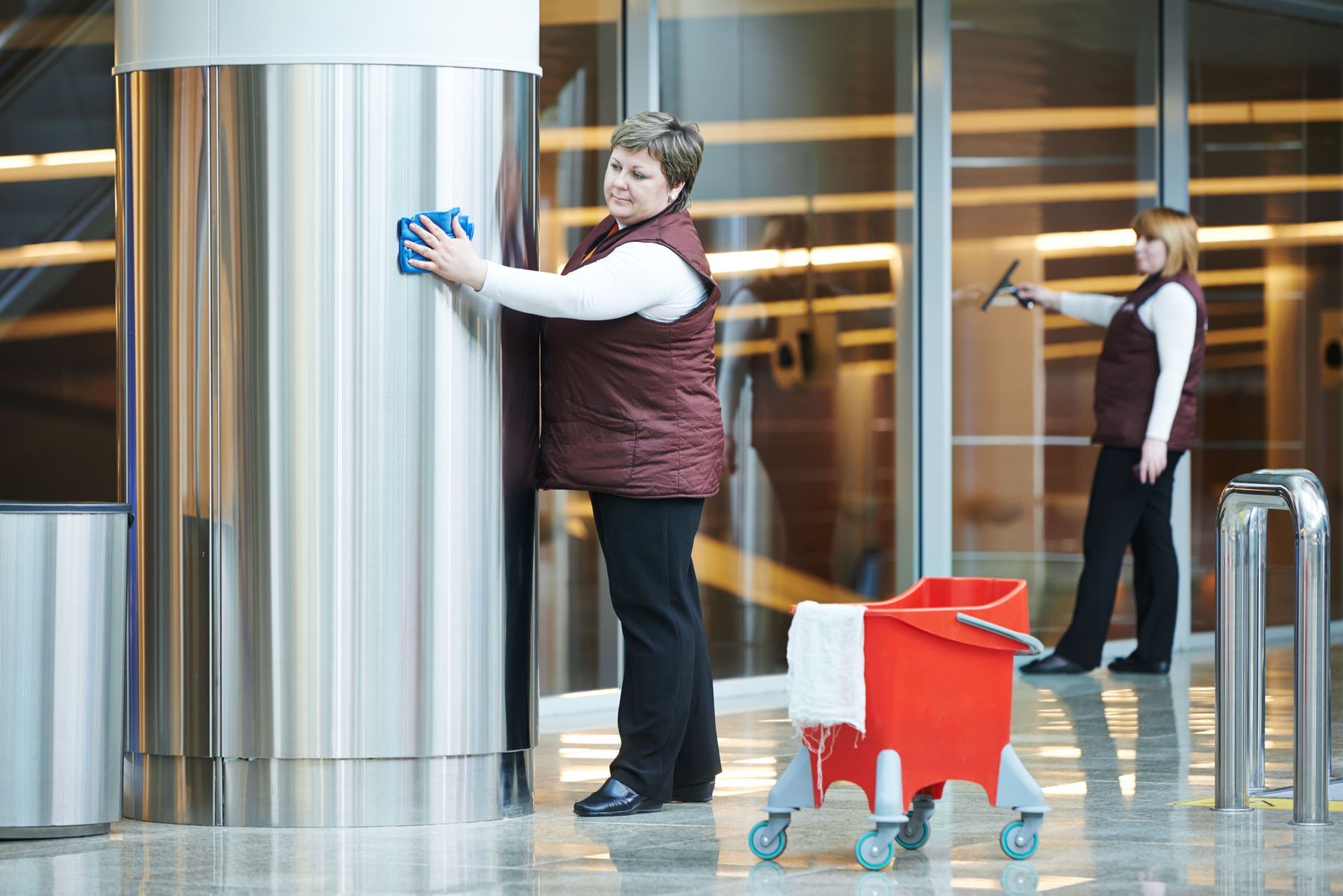 Two women are cleaning a building with a mop and bucket.