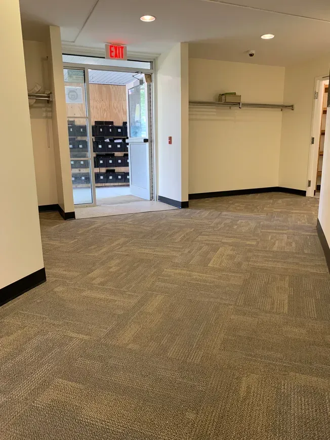 An empty hallway with a carpeted floor and a red exit sign.