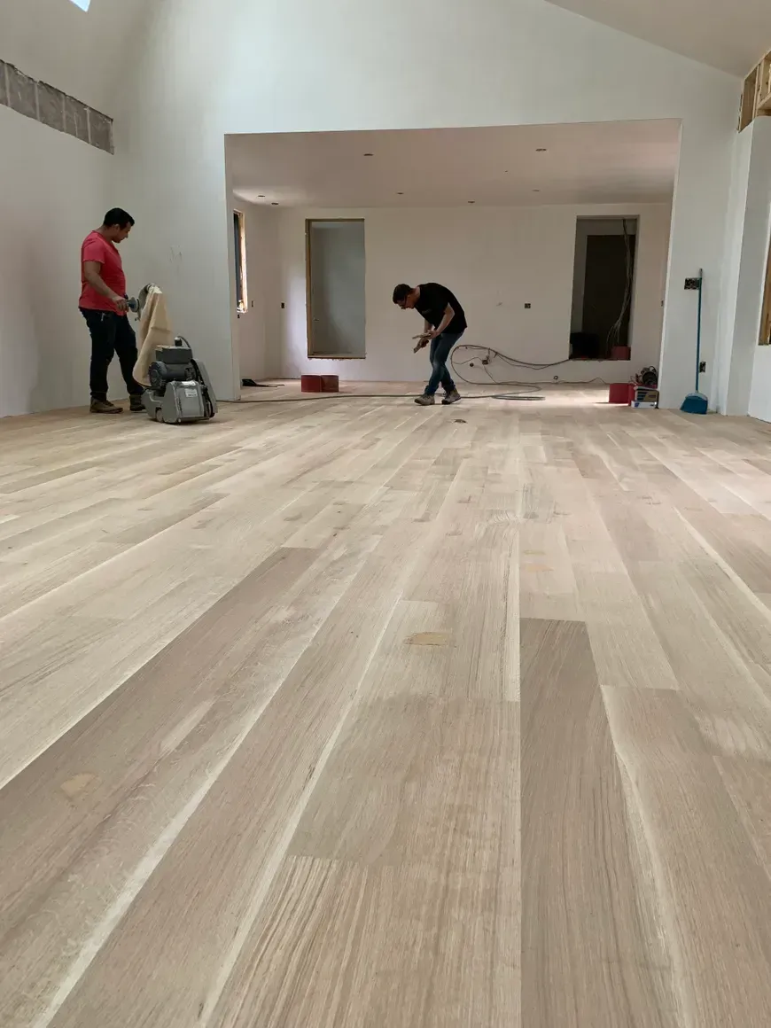 Two men are working on a wooden floor in a living room.