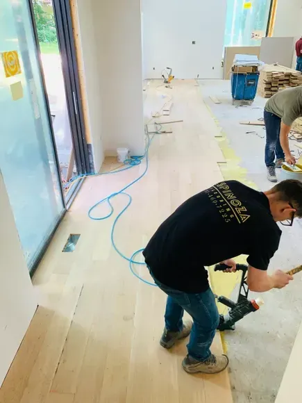 A man wearing a black shirt that says ' architectural ' on the back is working on a wooden floor
