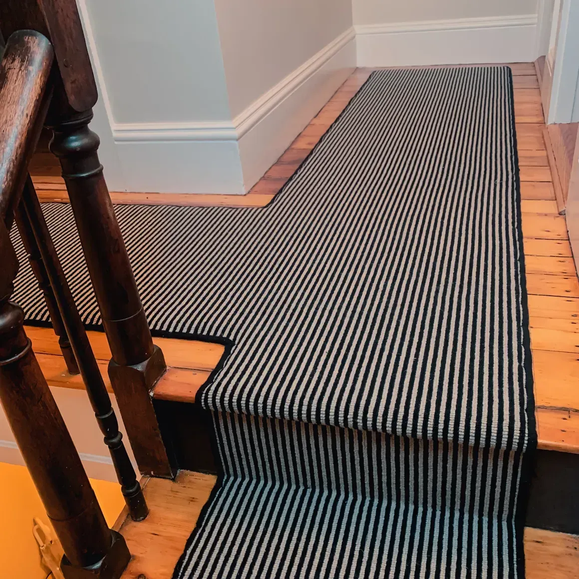 A wooden staircase with a black and white striped carpet