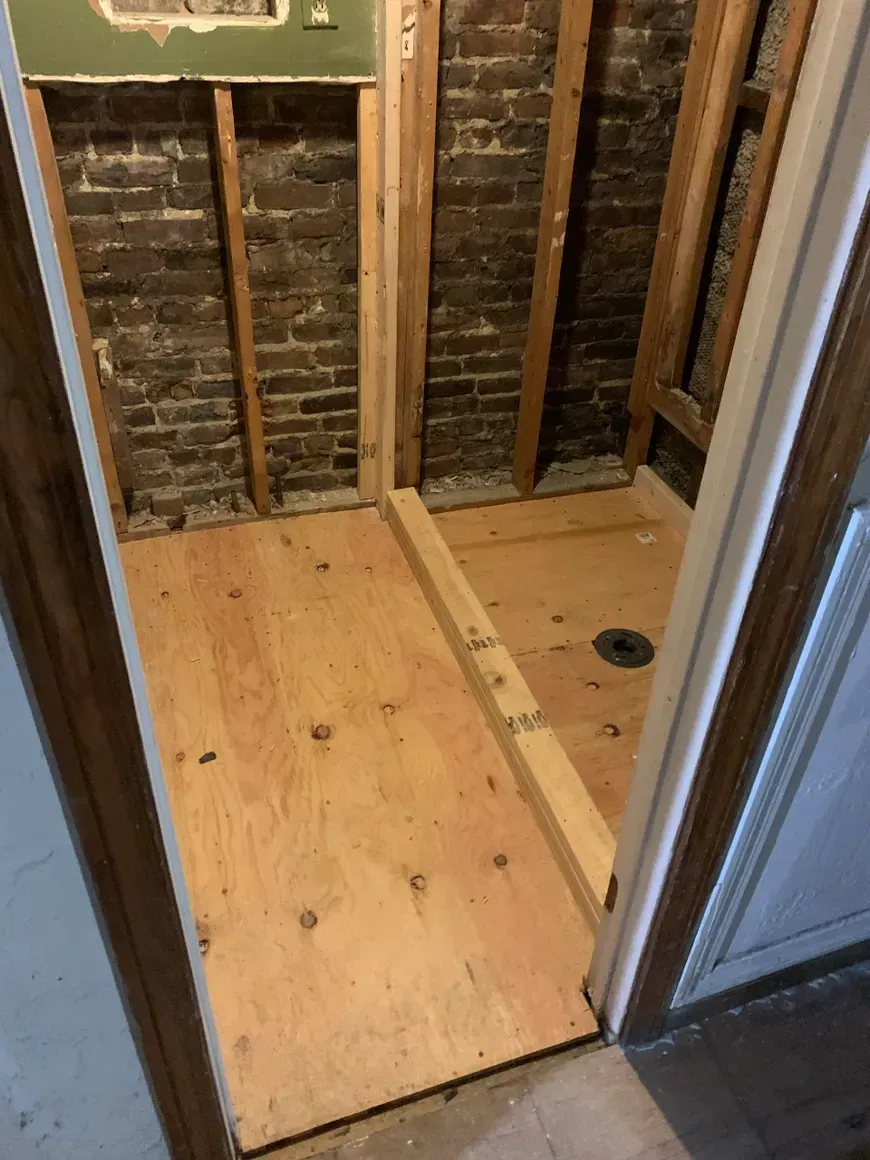A bathroom with a wooden floor and a brick wall.