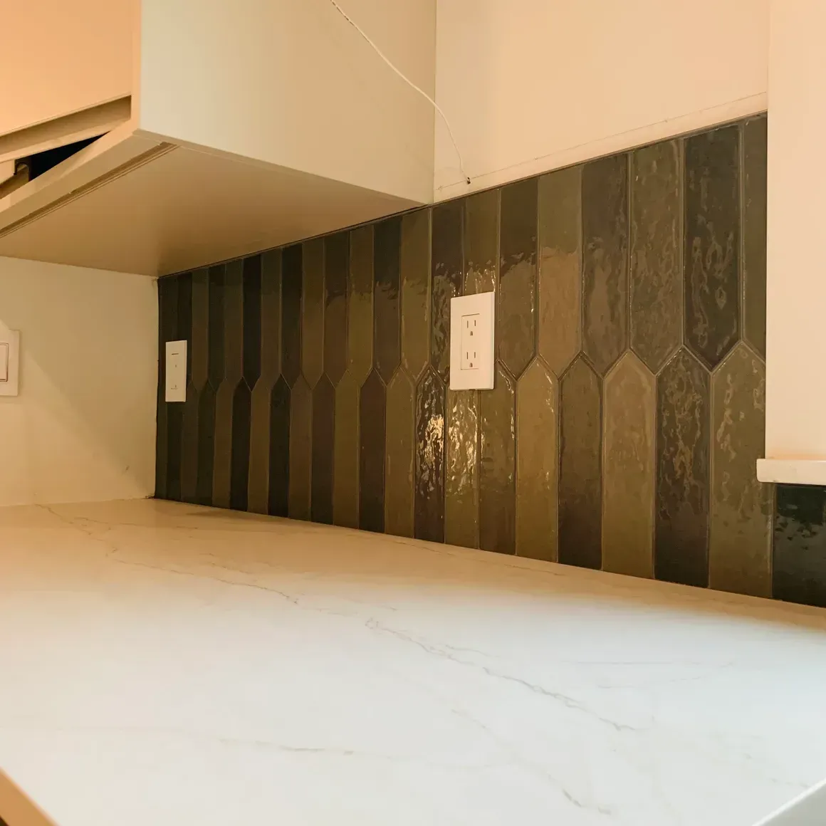 A kitchen with a counter top and a wall with tiles.