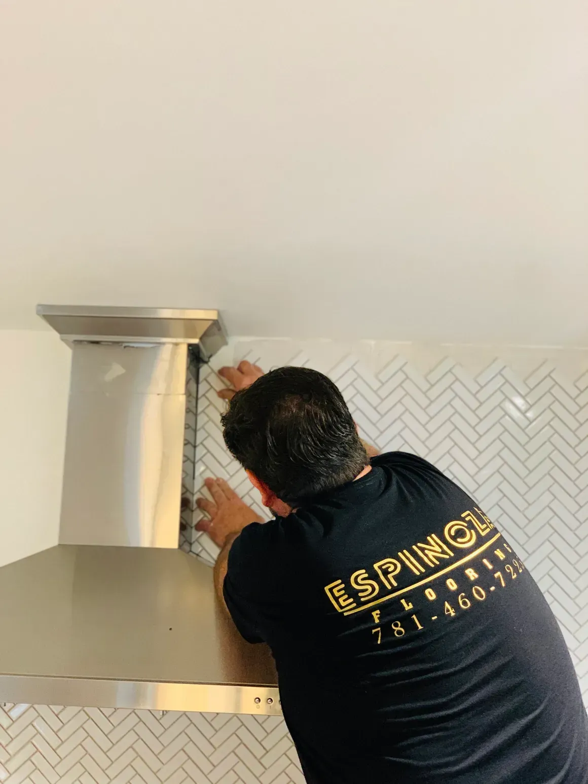 A man is installing a stainless steel hood in a kitchen.