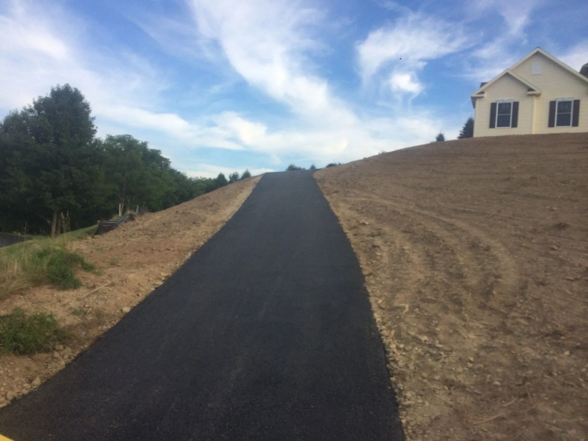 A paved road ascends a grassy hill towards a house under a cloudy sky.