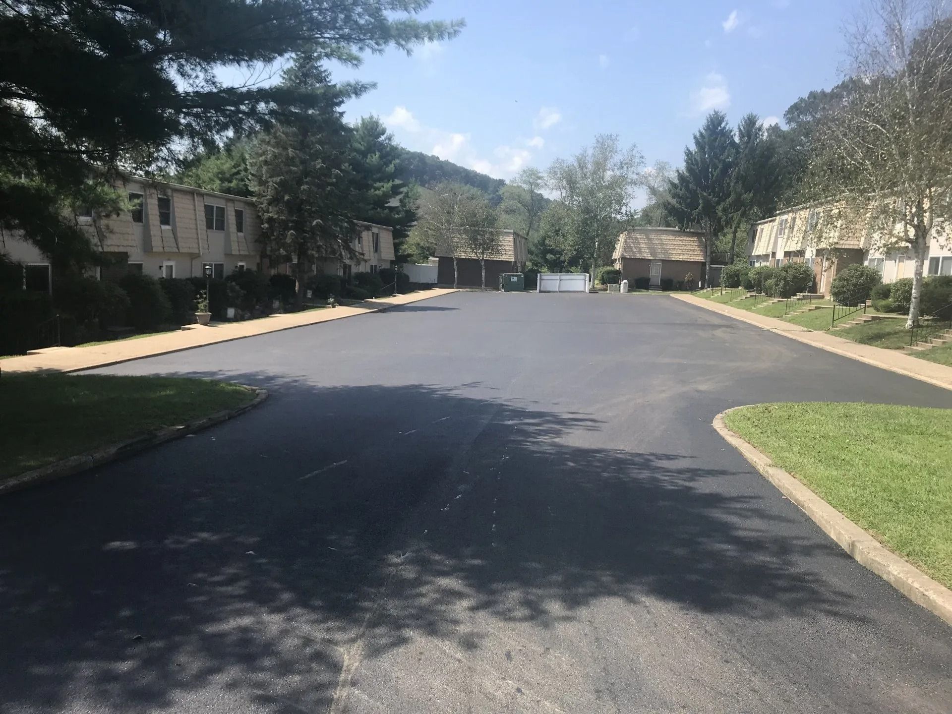 A newly paved asphalt parking lot with buildings and trees on a sunny day.