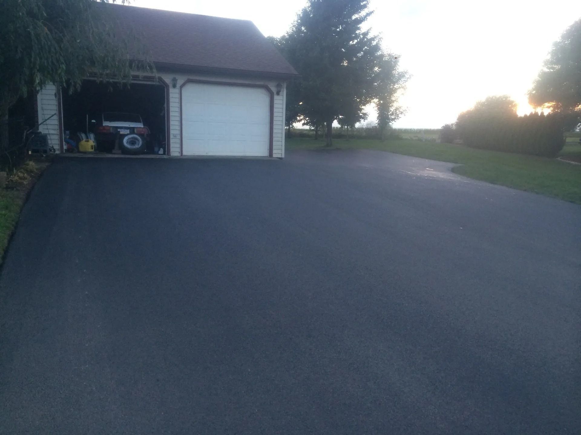 Newly paved black asphalt driveway in front of a two-car garage, with a vehicle inside.