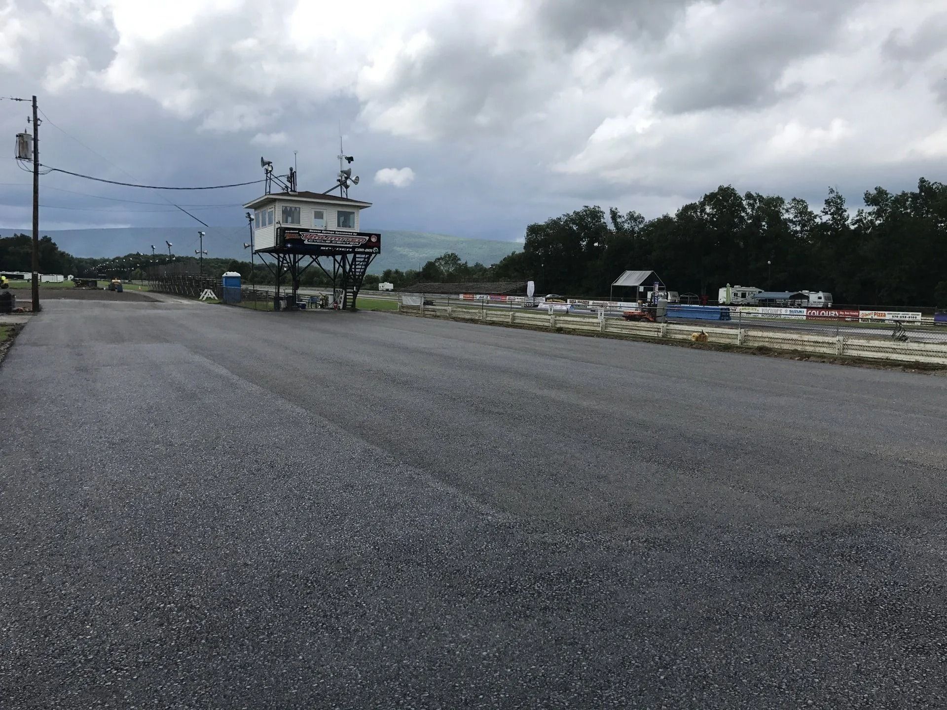 New asphalt road with control tower on stilts, overcast sky, trees in background.